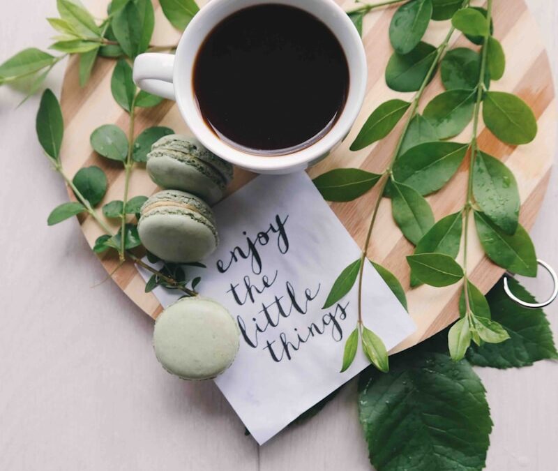 flat lay photography of leaves with cup of coffee and three macarons on chopping board