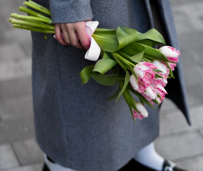 A person holds flowers, dressed in gray.