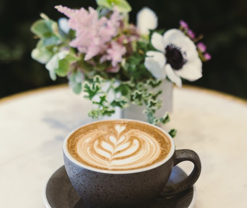 cup of cappuccino on saucer beside flower centerpiece